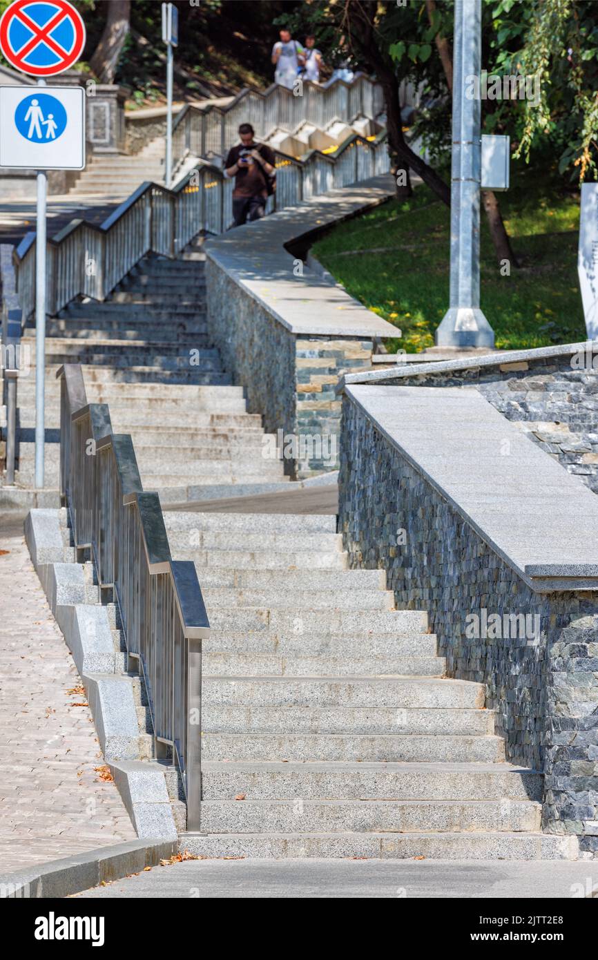 Granite stone stairs with metal railings lead up the slope in a modern city park on a sunny day. Vertical image. Stock Photo