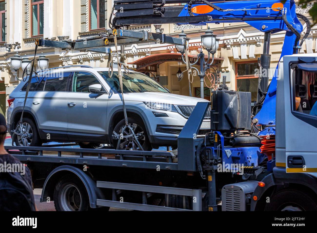 Loading a car on a tow truck on a narrow street of the old city on a sunny summer day. Stock Photo