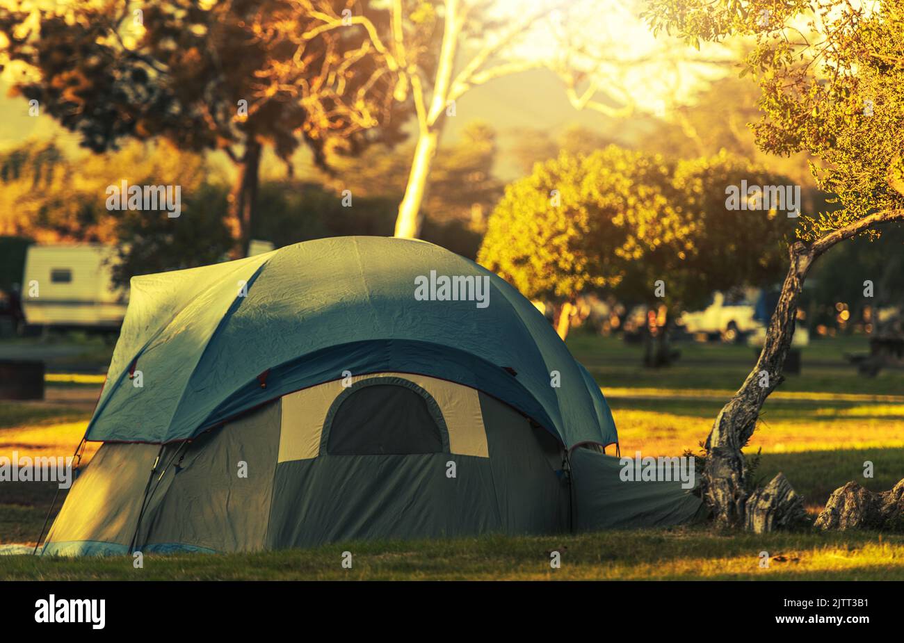 Modern Tent in Khaki Green Color with Additional Roof Protector Cover Pitched and Secured on a Campground. Fall Foliage in the Background. Camping and Stock Photo