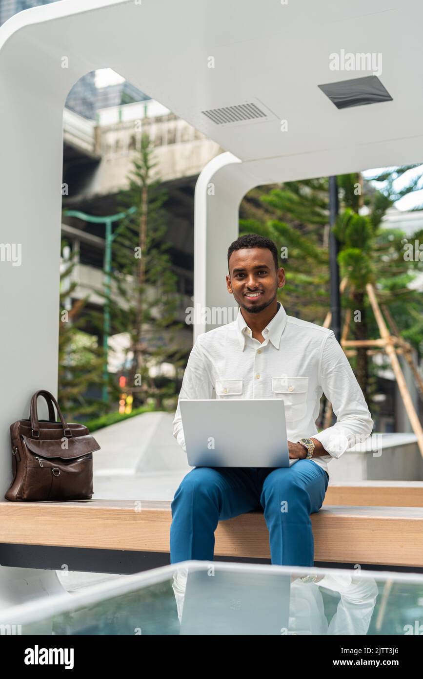 Portrait of young handsome stylish black man using laptop computer in city Stock Photo