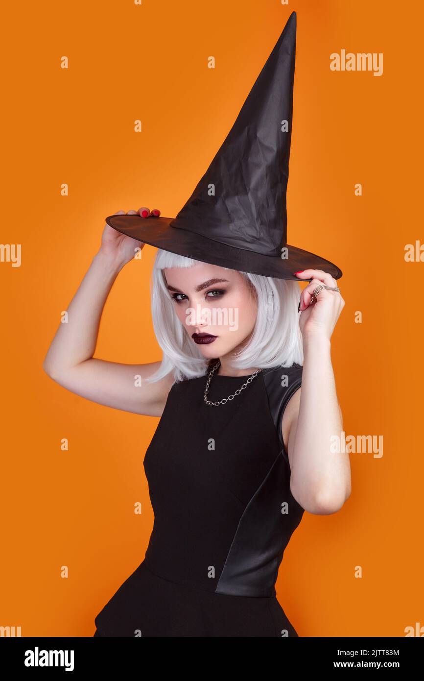 Young woman dressed like a witch posing on orange background. Happy Halloween Stock Photo