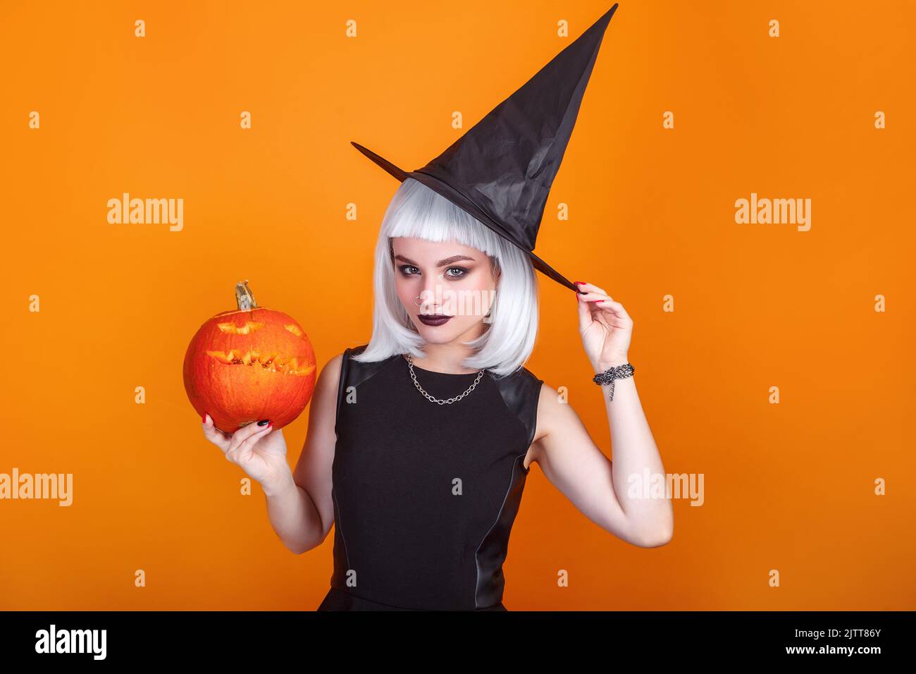 Beautiful sexy woman in witch hat and costume holding carved pumpkin. Happy halloween Stock Photo