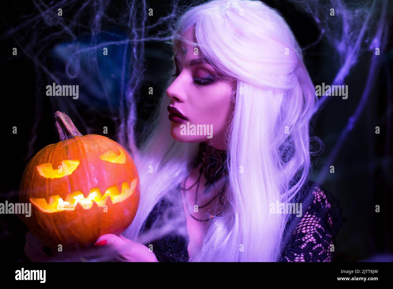 Sexy witch with hallowen makeup and long white hair holding pumpkin on black background Stock Photo