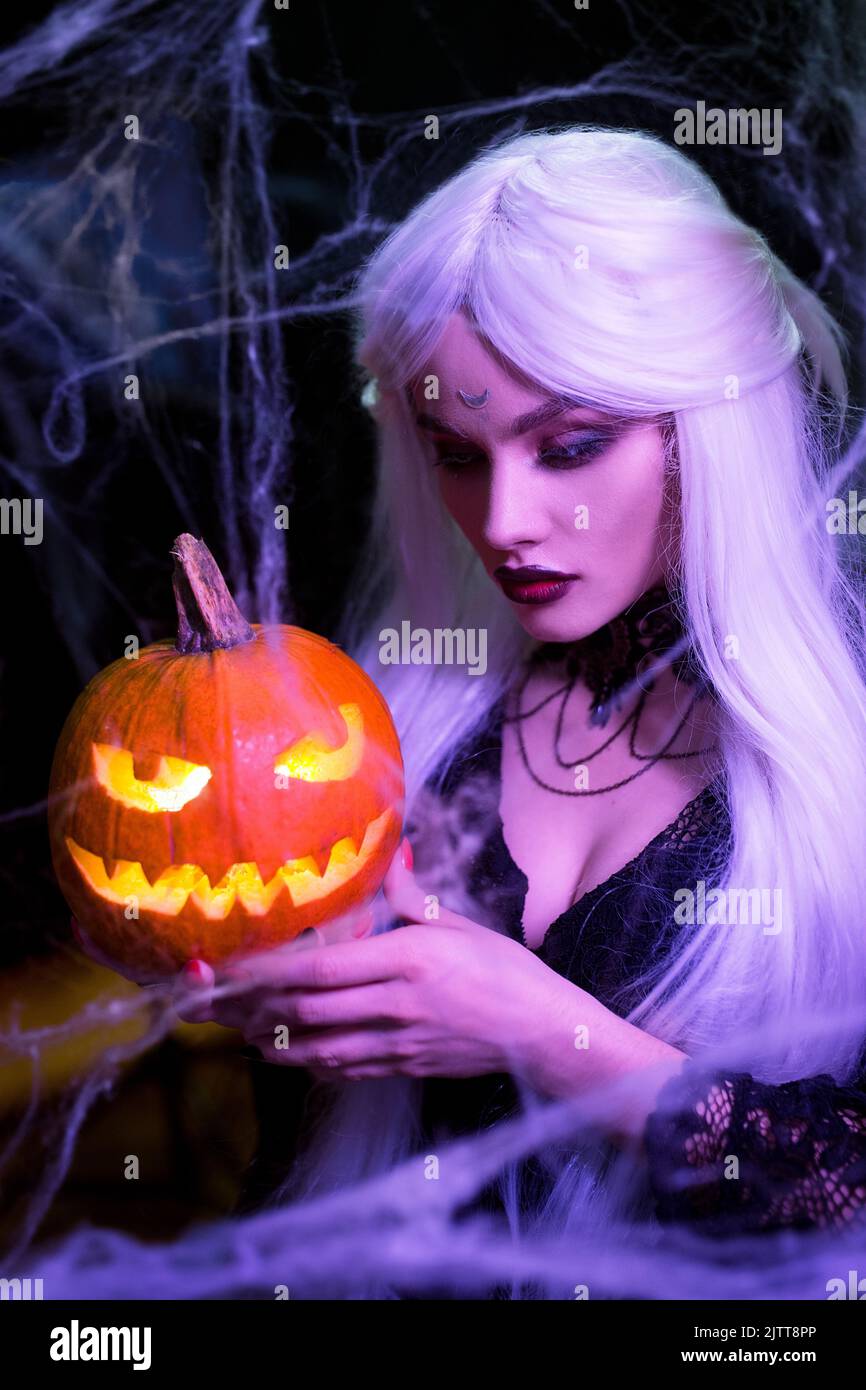 Sexy witch with hallowen makeup and long white hair holding pumpkin on black background Stock Photo
