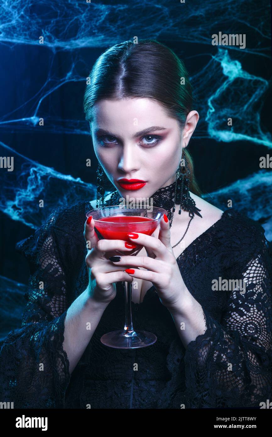 Halloween vampire woman portrait with a glass of wine on dark magic background Stock Photo
