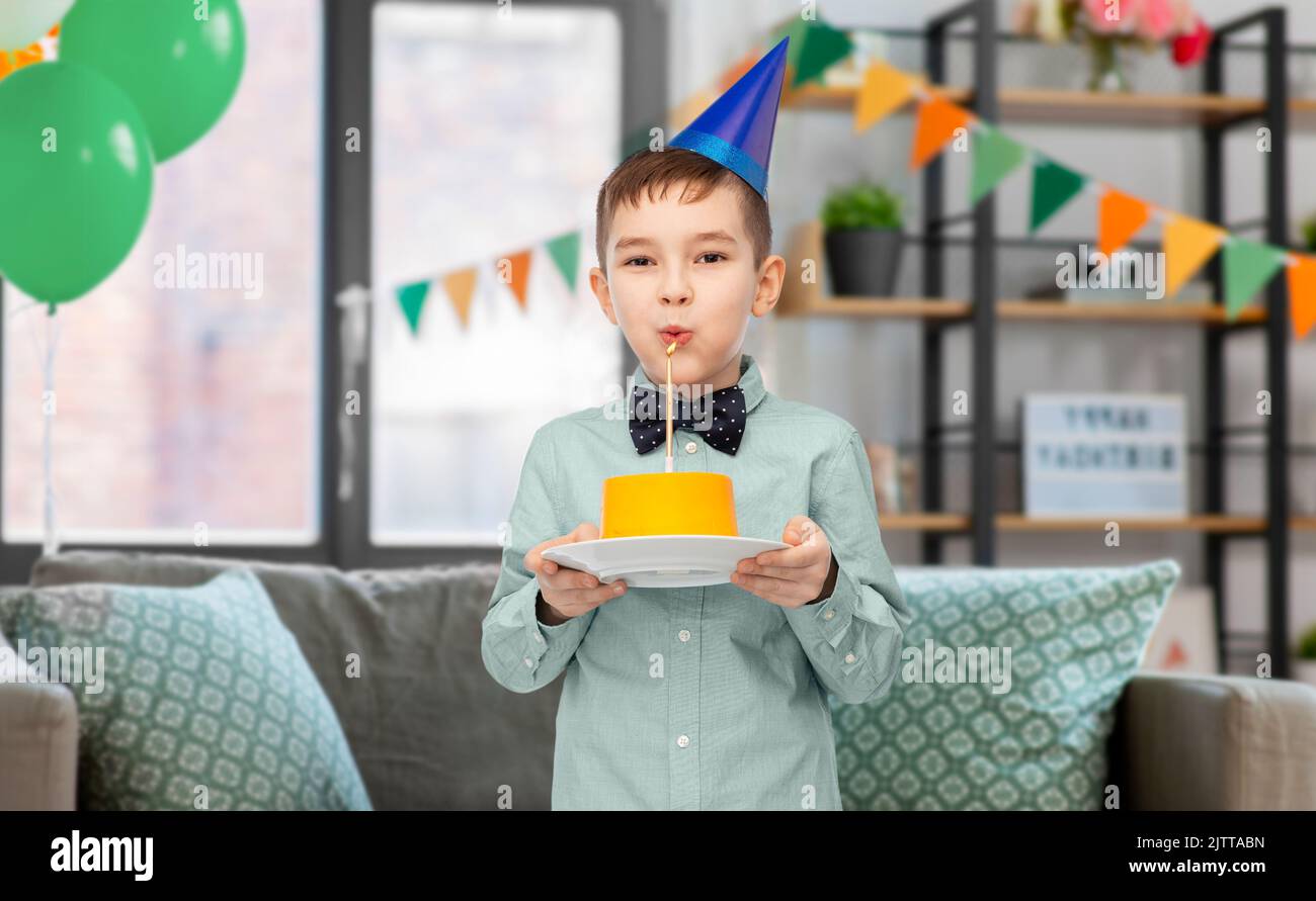 boy in party hat blowing candle on birthday cake Stock Photo - Alamy