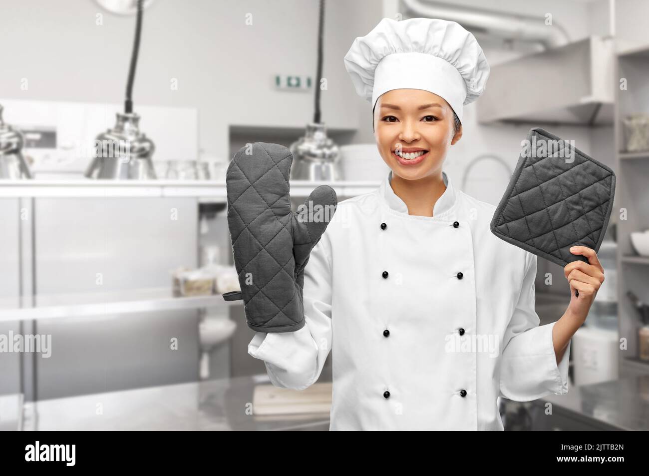 smiling female chef with potholders in kitchen Stock Photo