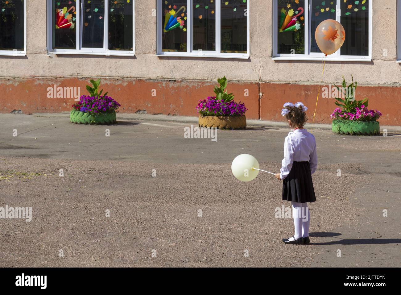 A lonely schoolgirl with two balloons is waiting for an invitation to a solemn event at school on the first of September. Stock Photo