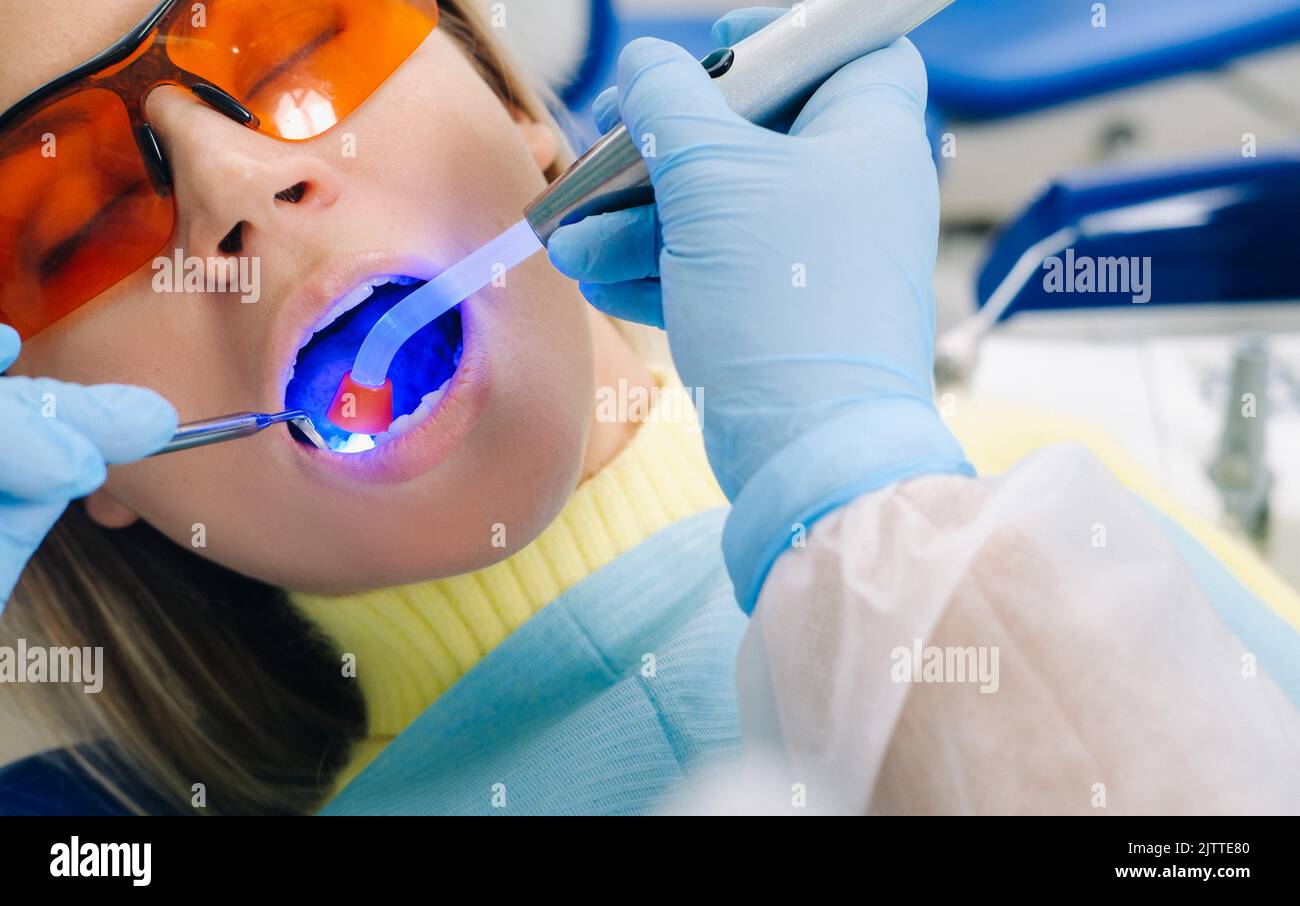 A young beautiful girl in dental glasses treats her teeth at the