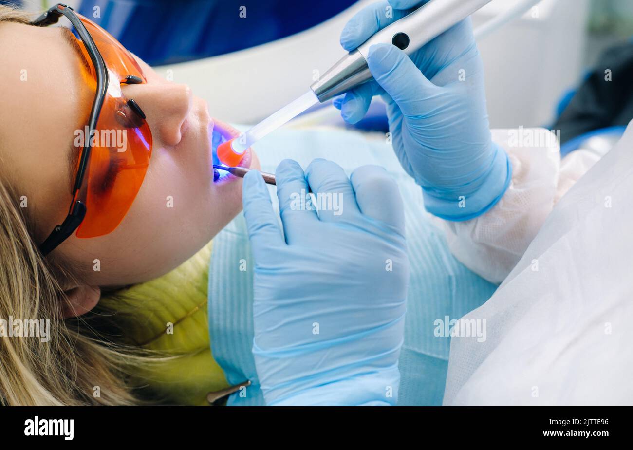 A young beautiful girl in dental glasses treats her teeth at the