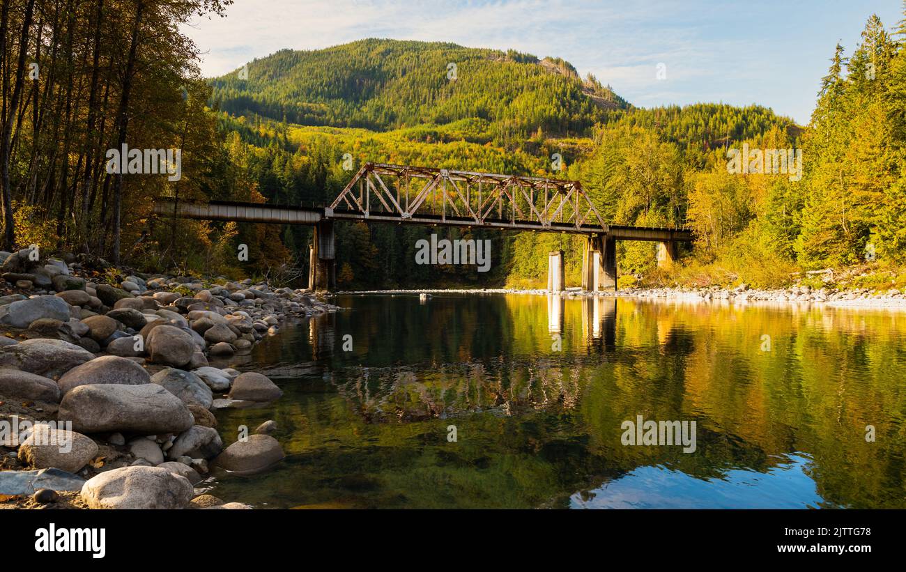 Skykomish River reflecting the railway bridge as the trees begin to turn fall colors in Western Washington State Stock Photo