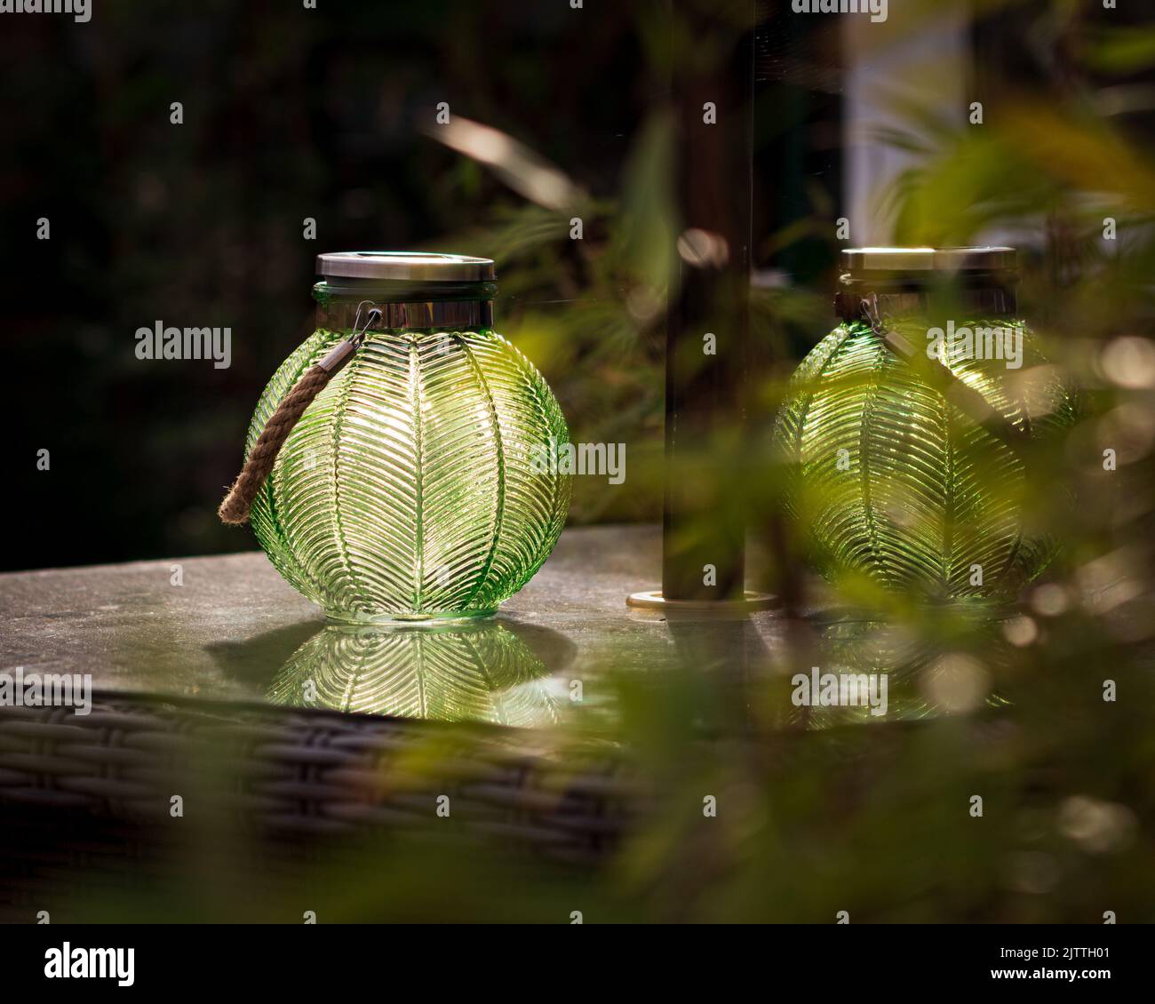 A beautiful shot of green, striped, round glass solar lantern on table on terrace on summer evening Stock Photo
