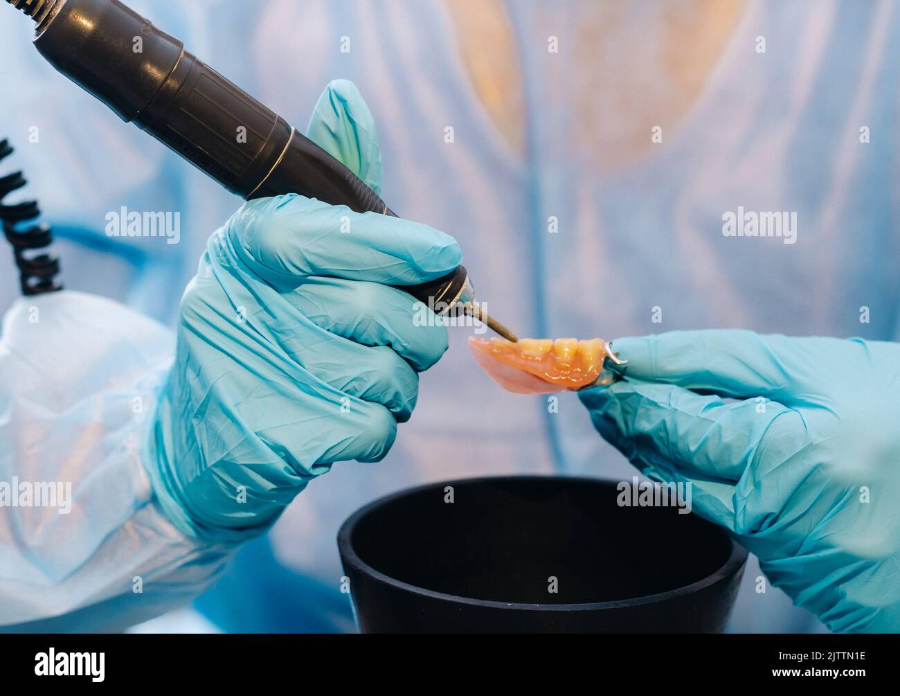 A masked and gloved dental technician works on a prosthetic tooth in