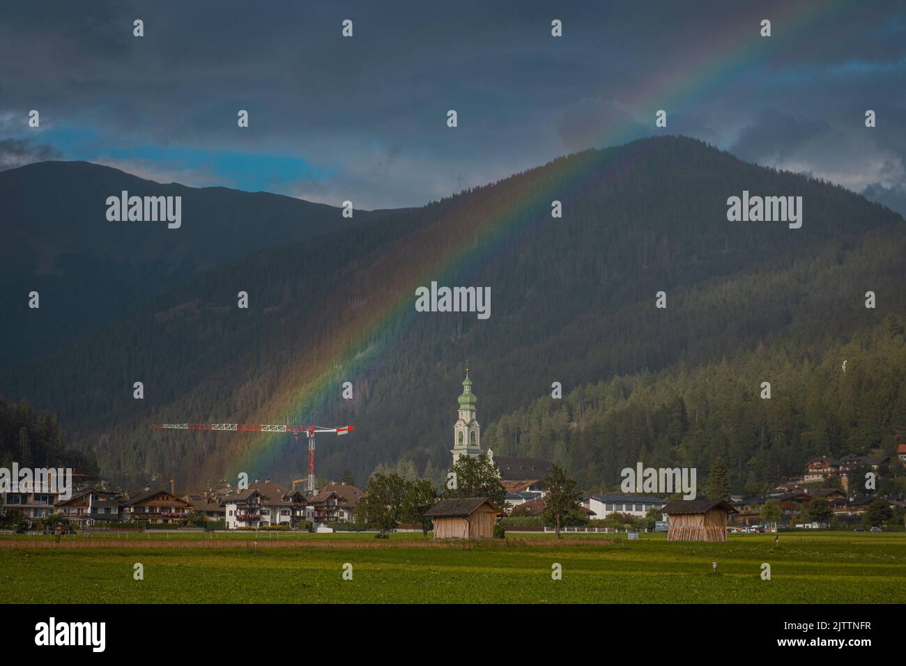 Beautiful rainbow rising above the houses and church in Toblach or Dobbiaco, a small town in austrian part of northern italy. Stock Photo