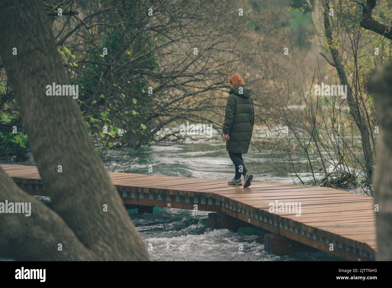 Unknown woman walking on the wooden path or walkway over some water rapids. Dangerous walking, suicidal tendencies. Stock Photo