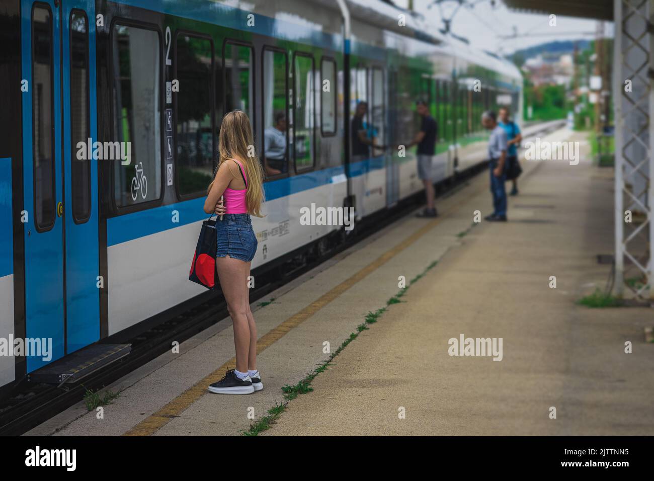 Young female is ready to hop on a train, waiting in front of the door, ready to enter. Nice young woman with sexy jeans shorts waiting for a train. Stock Photo