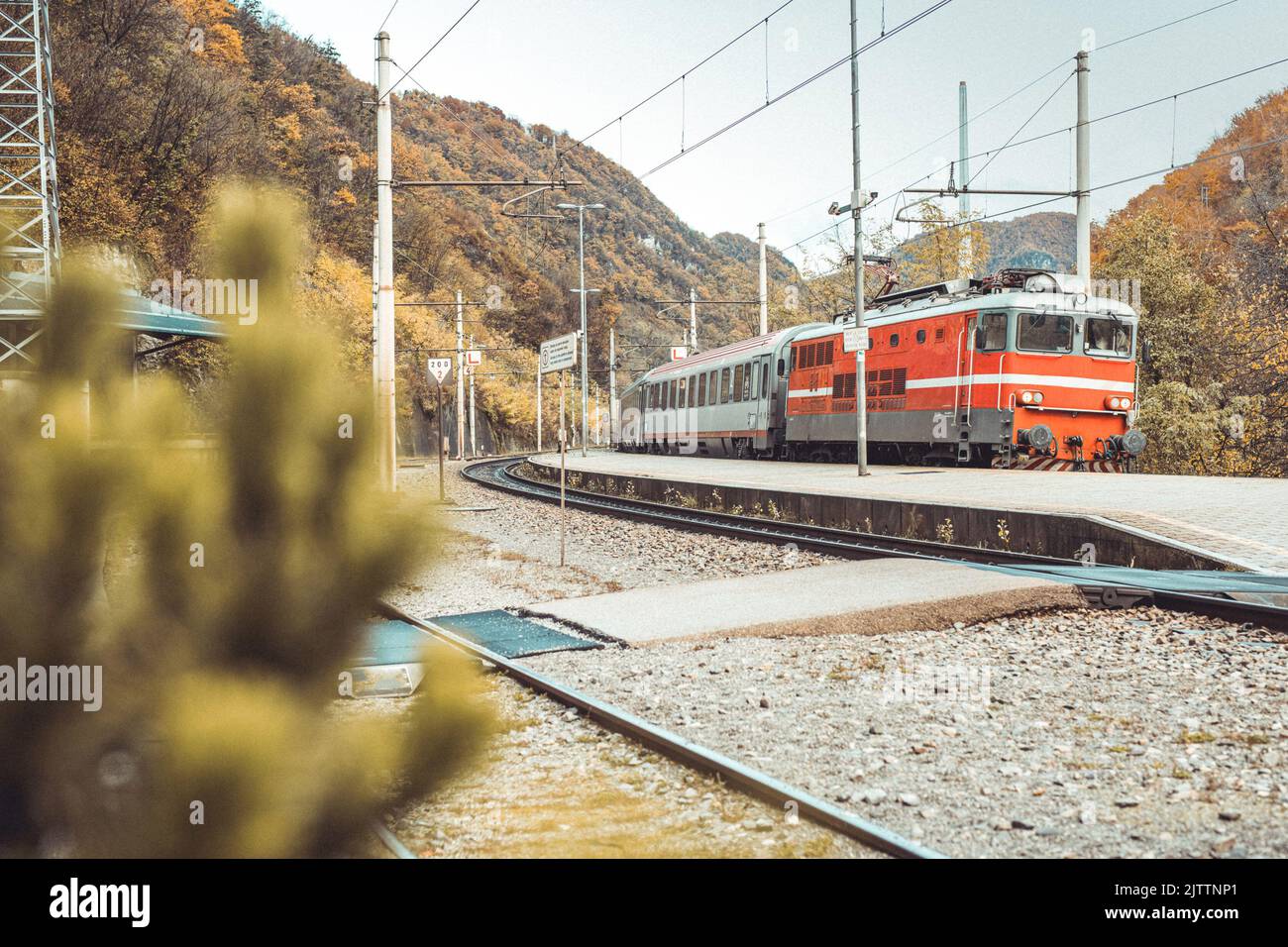 Passenger train with red locomotive rushing through the station of Trbovlje in early autumn. Stock Photo