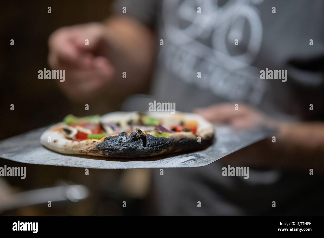 Man holding a burnt home made pizza in his hand. Pizza dough being burnt. Delicious pizza in home oven. Stock Photo