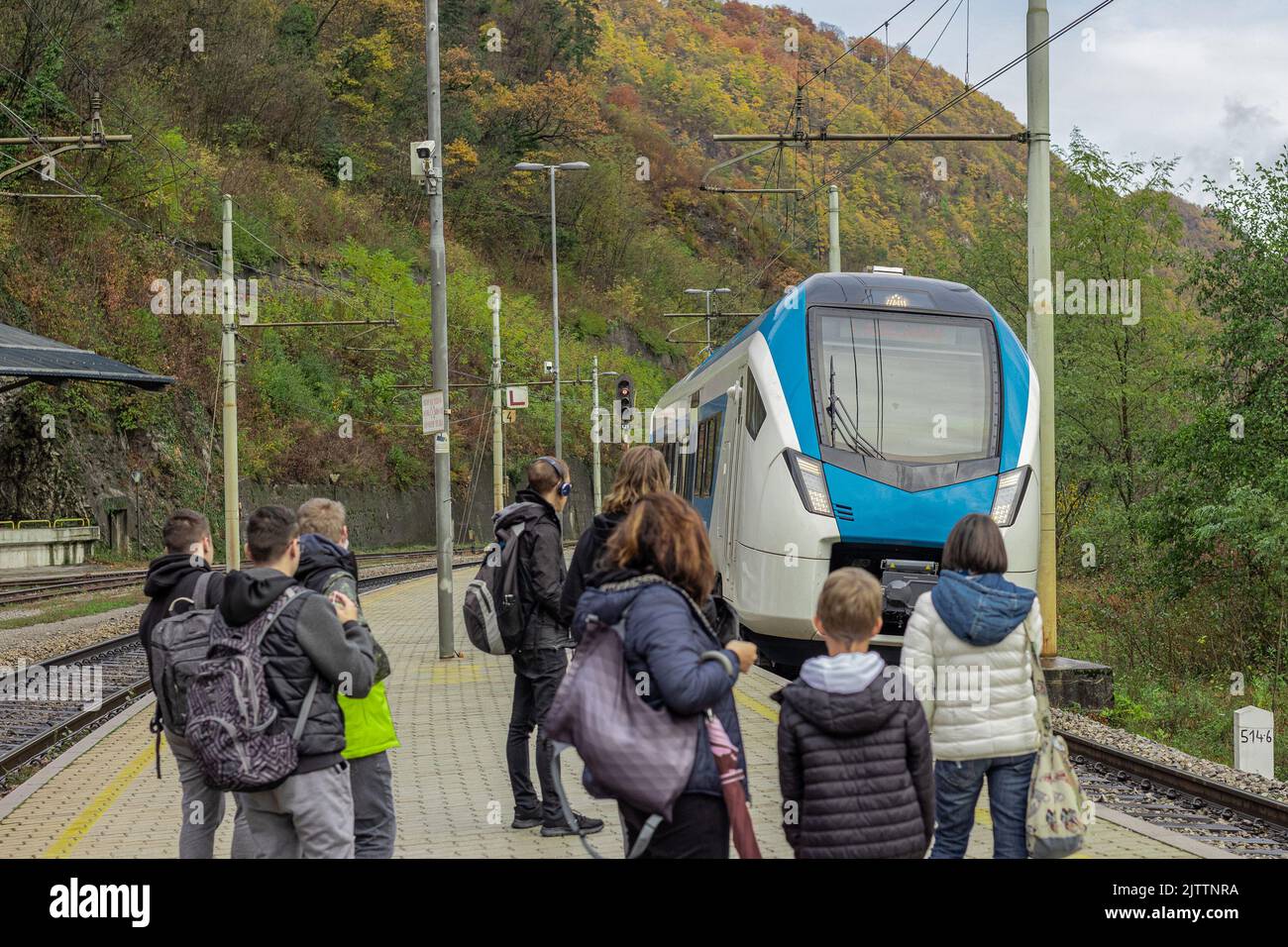 Unknown passengers are waiting at a train platform for a modern white and blue train to arrive to the station. Trbovlje, slovenia. Stock Photo