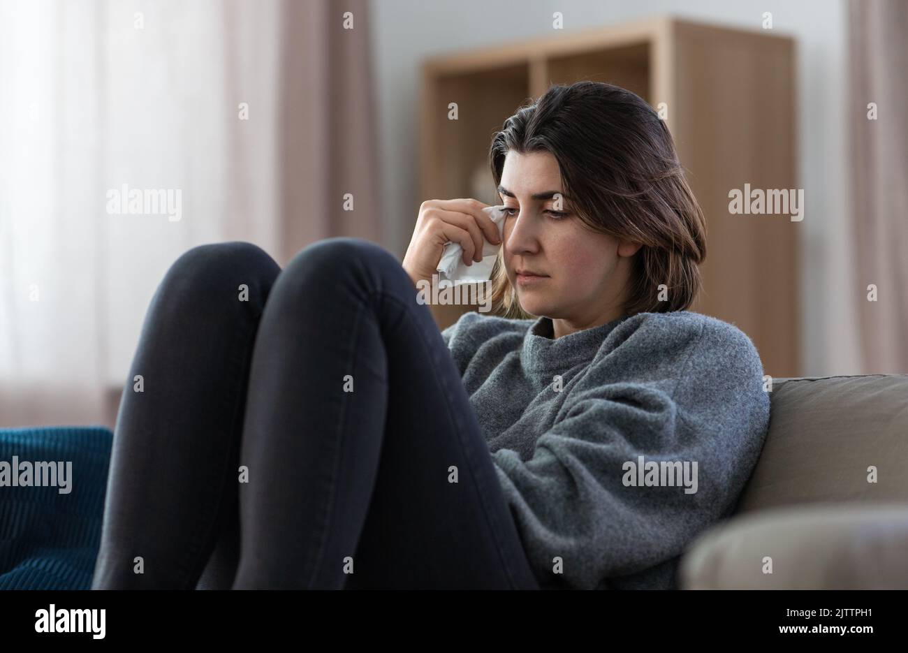 sad crying woman sitting on sofa at home Stock Photo