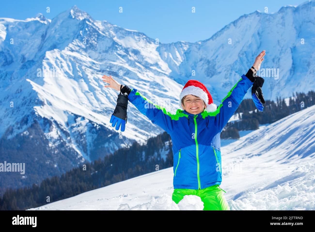 Boy with Santa hat and big smile stand in snow lift up hands Stock Photo