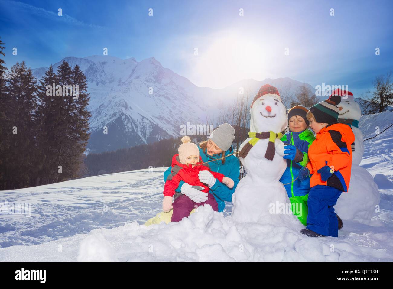 Family with mother, girl and two boys build, dress snowman Stock Photo