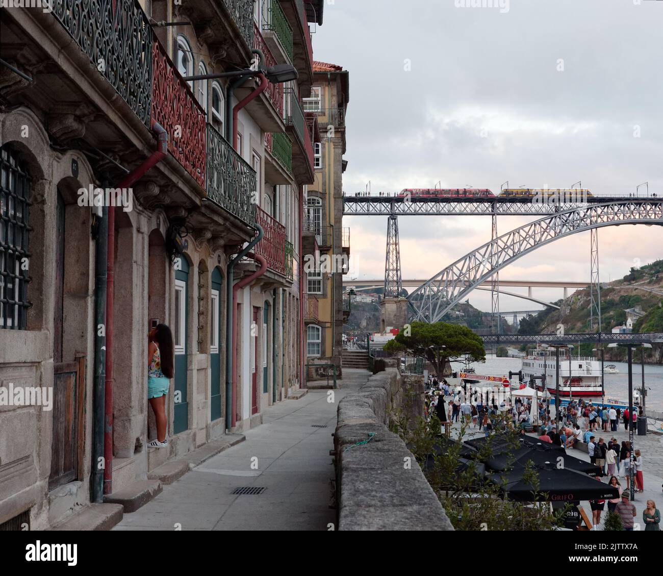 Properties with balconies on a raised walkway in the Riberia district of Porto with the Douro river and a metro train on the Luis I bridge. Portugal Stock Photo