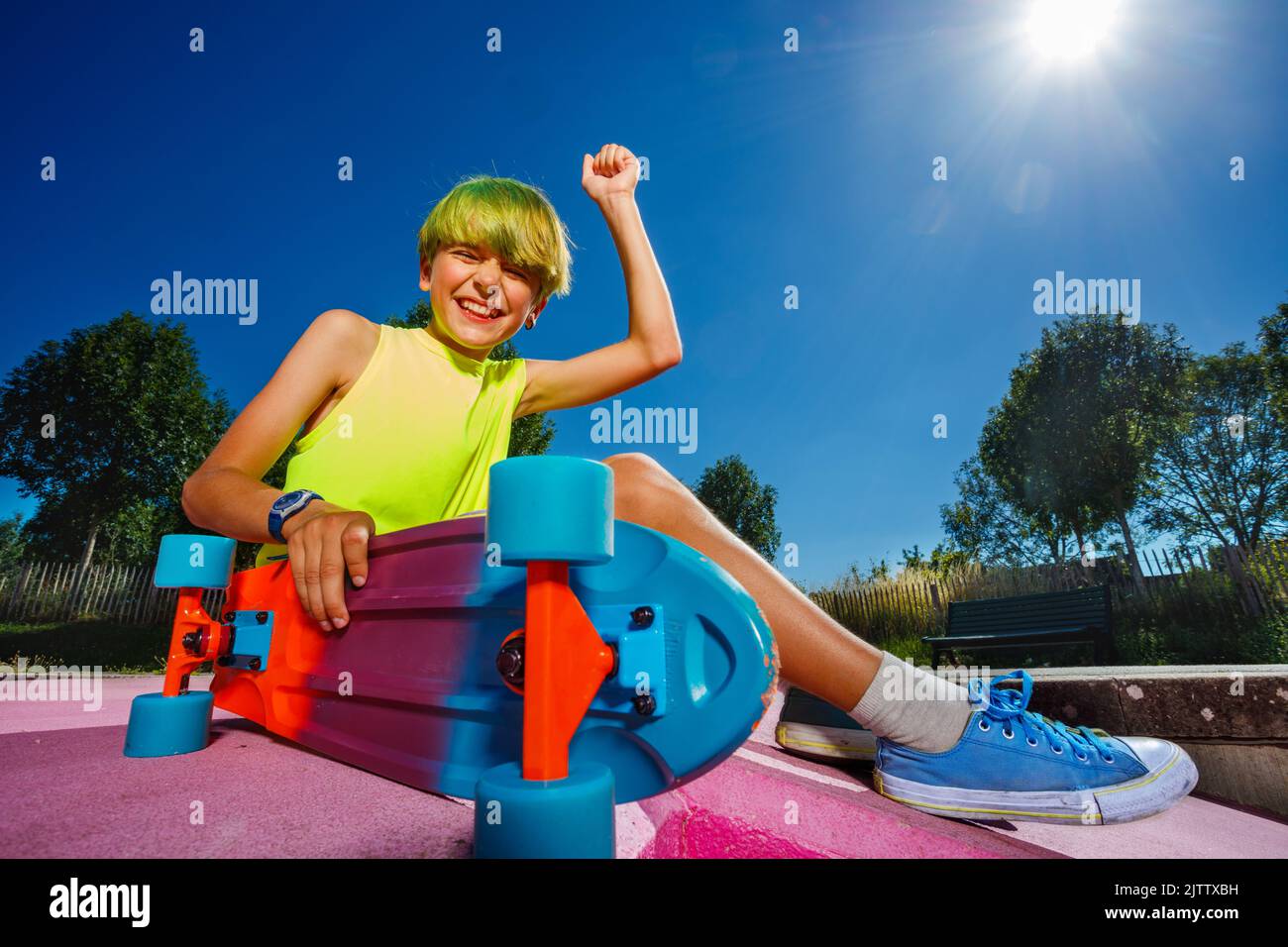 Cute skater boy with yes gesture sit holding skateboard in park Stock Photo