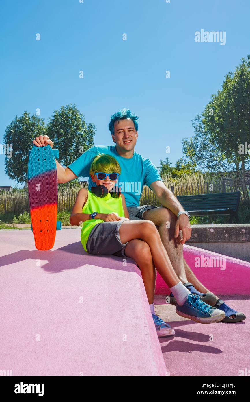 Father with blue hair sit together by son holding skateboard Stock Photo