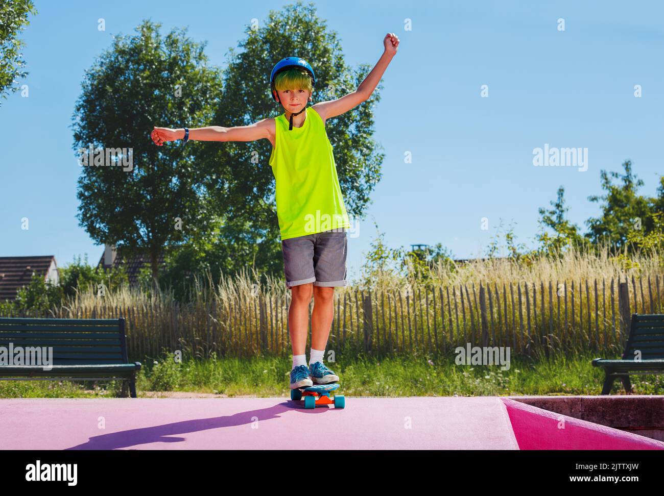 Child with green hair ride skateboard at skatepark stretch hands Stock Photo