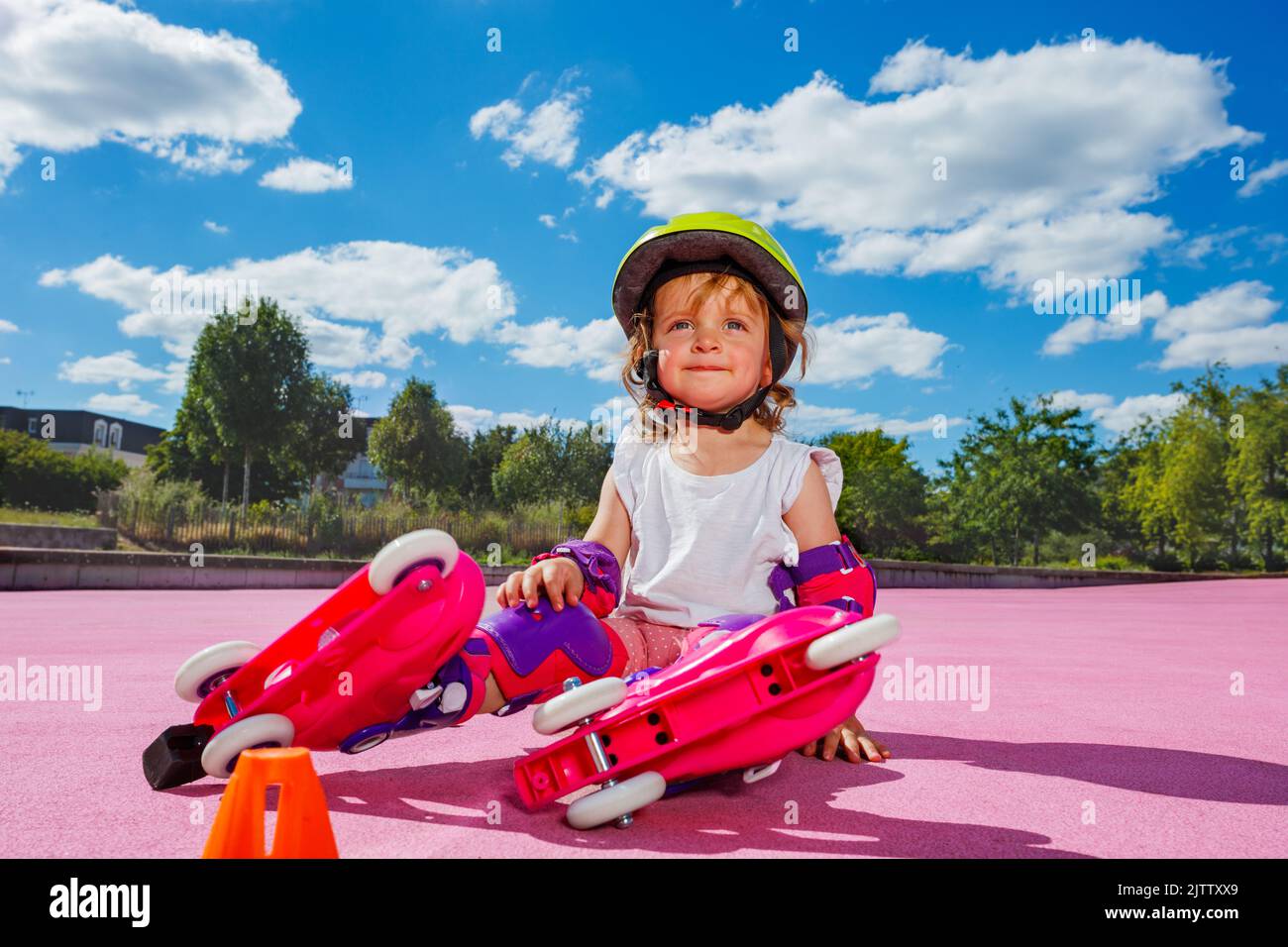 Girl learn rollers, sit in protection on color floor of the park Stock Photo