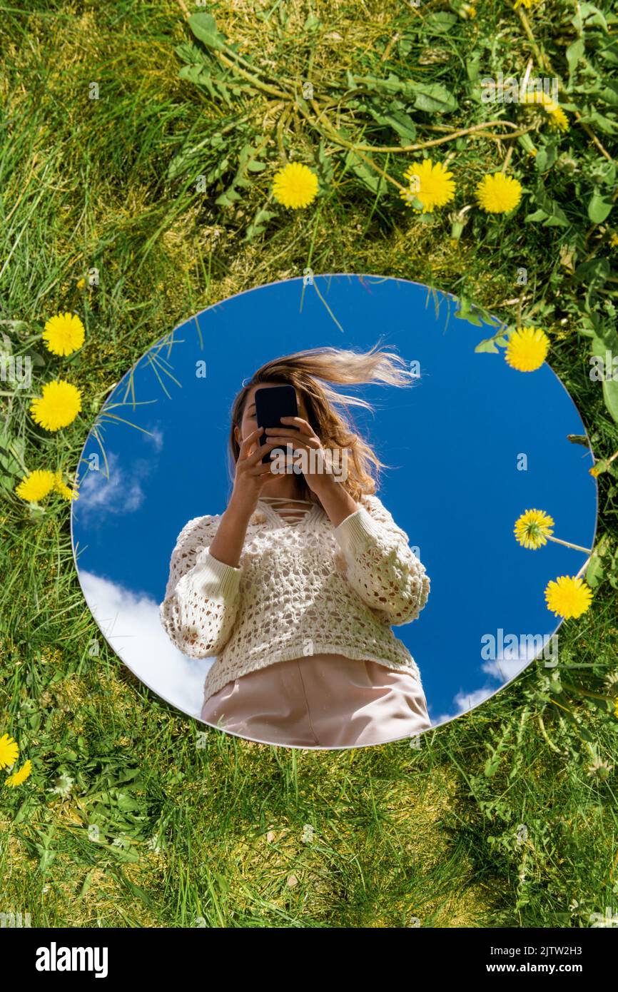 woman with smartphone reflection in round mirror Stock Photo