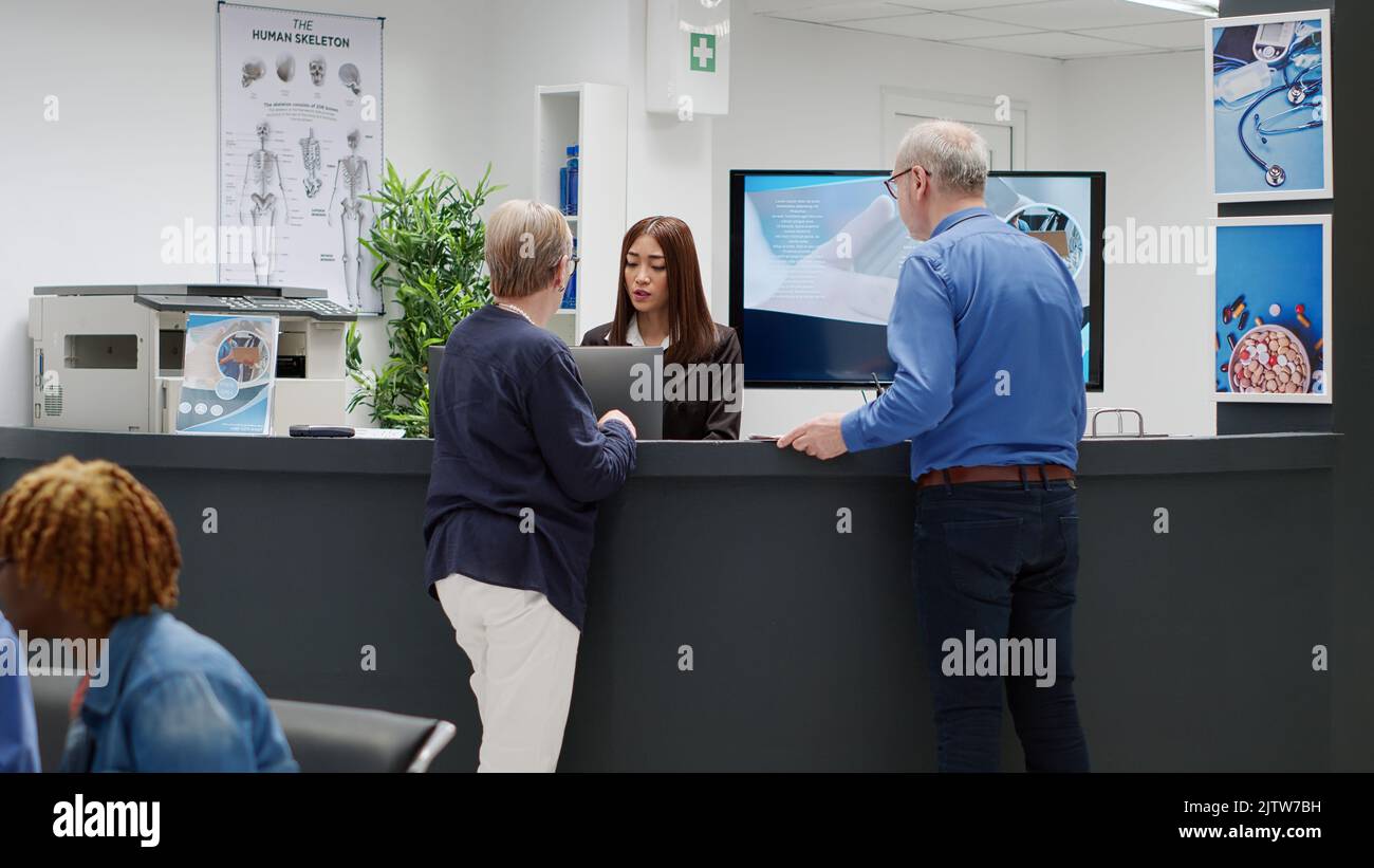 Senior people talking to receptionist at hospital reception desk ...
