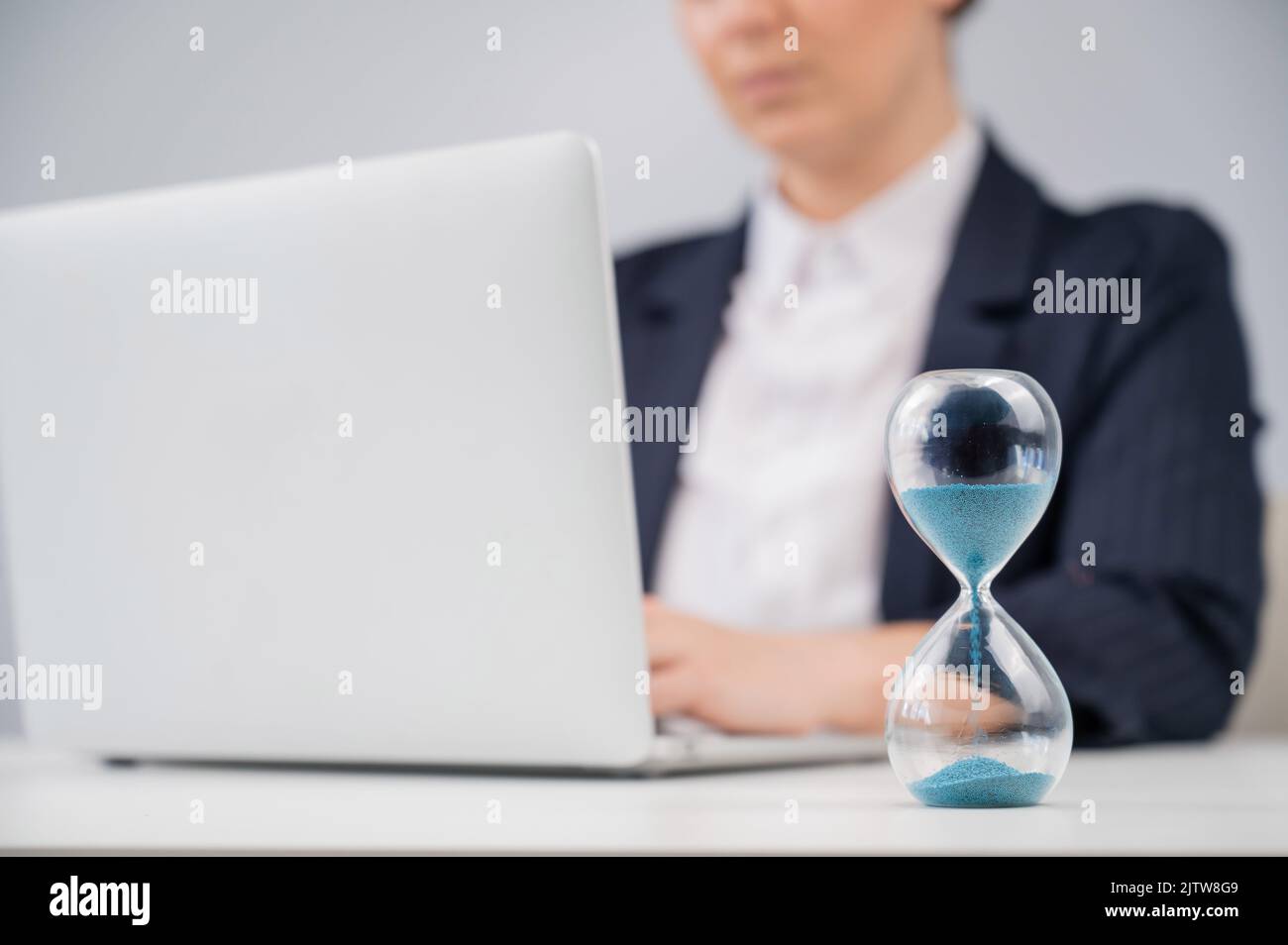 Business woman keeps track of time on an hourglass while working Stock