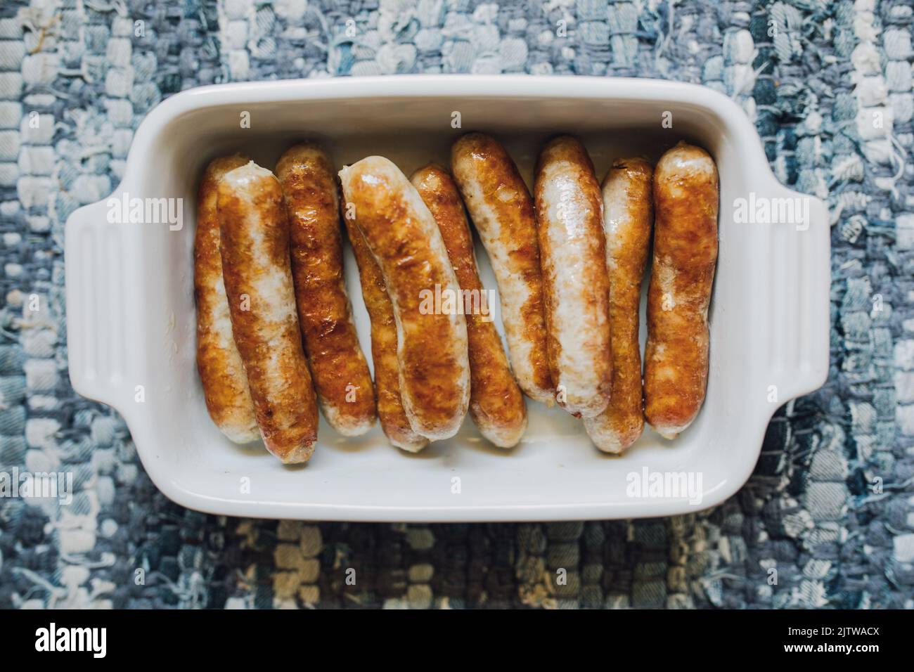 bbrowned, cooked individual breakfast sausage links in white dish on blue placemat, table Stock Photo