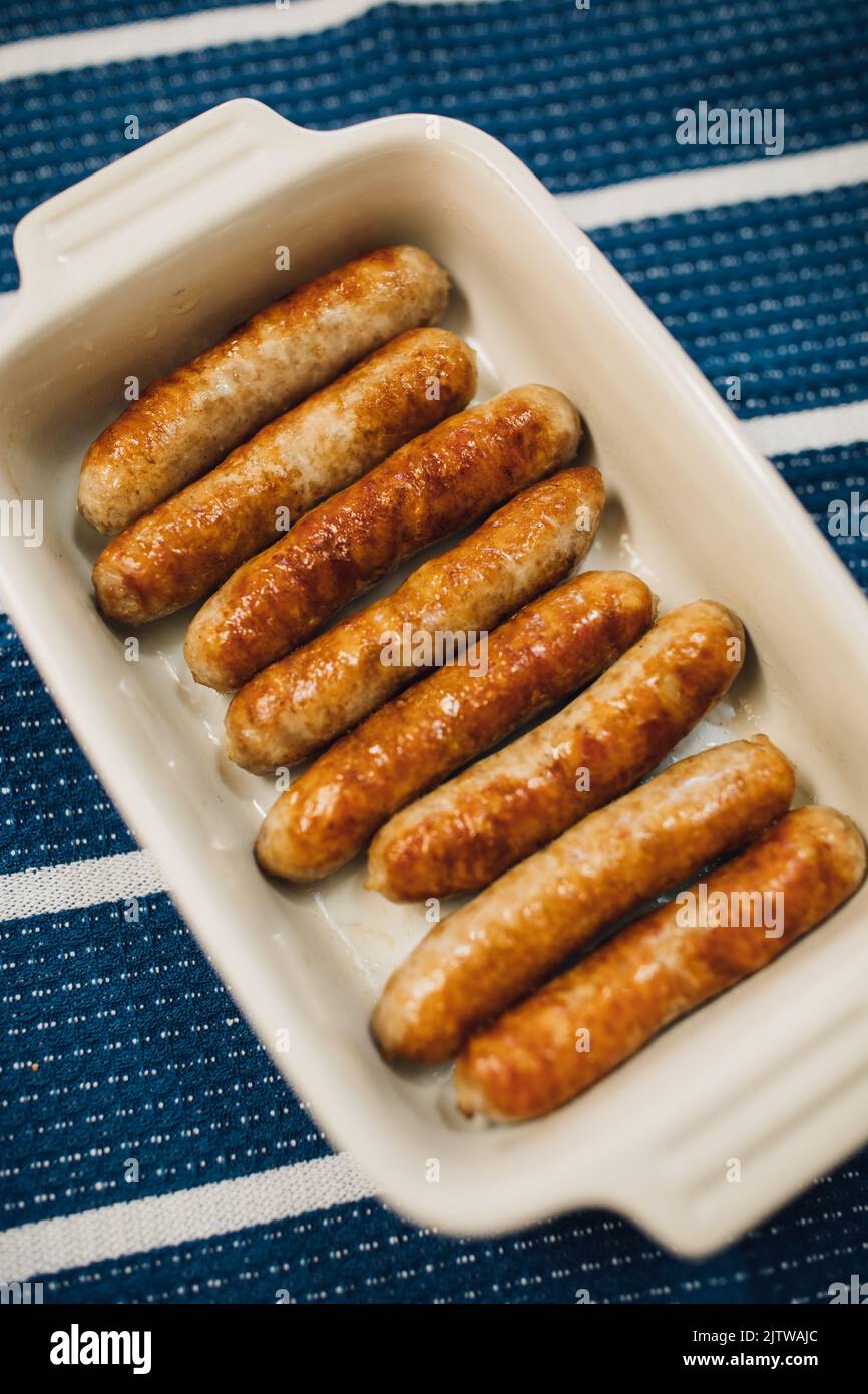 browned, cooked individual breakfast sausage links in white dish on blue and white stripe cloth Stock Photo