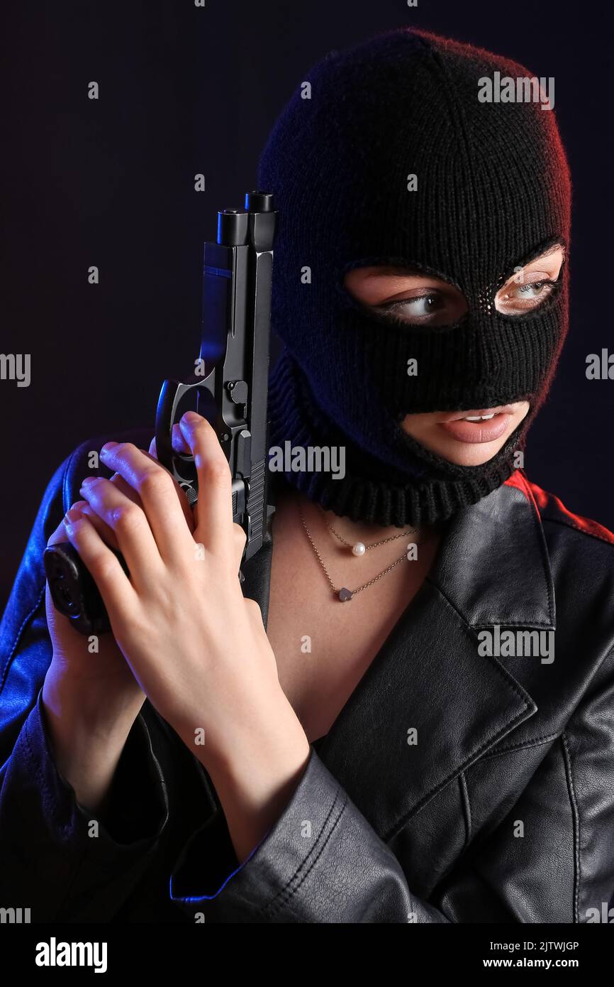 Portrait of young woman in balaclava and leather jacket with gun