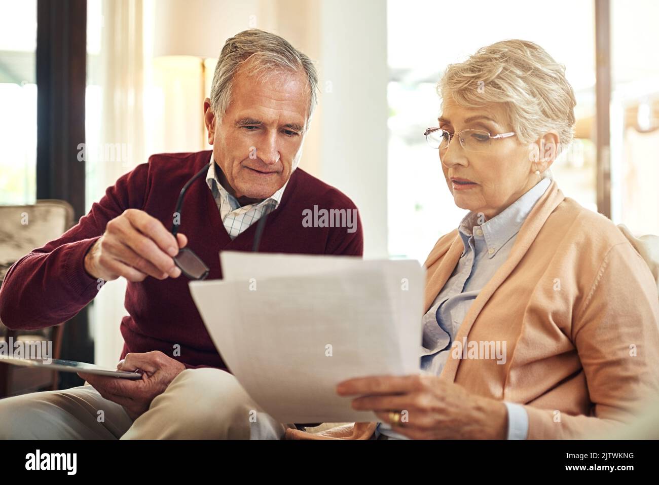 They believe in keeping track of all their expenses. an elderly couple working out a budget while sitting on the living room sofa. Stock Photo