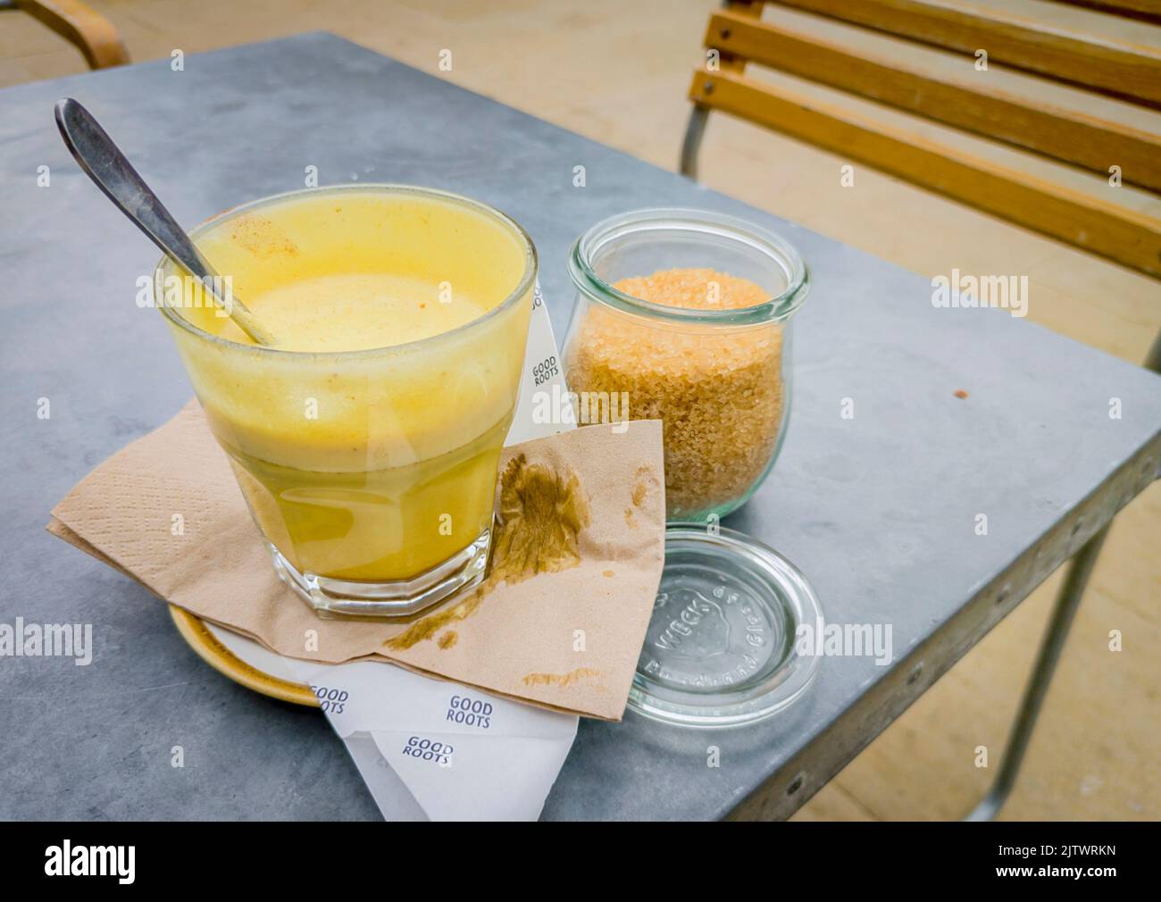 Sweet yellow tinted coffee,served in a glass,with a spoon after being stirred with demerara sugar,set outdoors on a restaurant table. Stock Photo