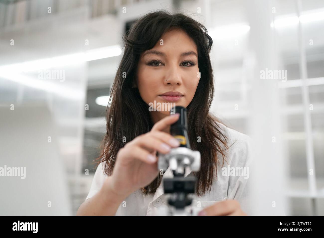 Young scientist in white lab coat working with binocular microscope in the material science lab