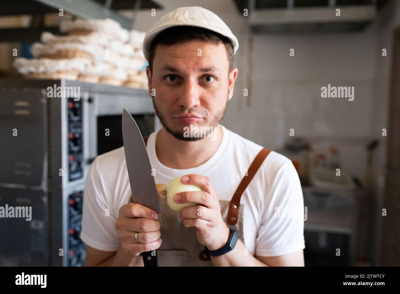 A baker is peeling onions in a small artisan bakery. Front view. Stock Photo