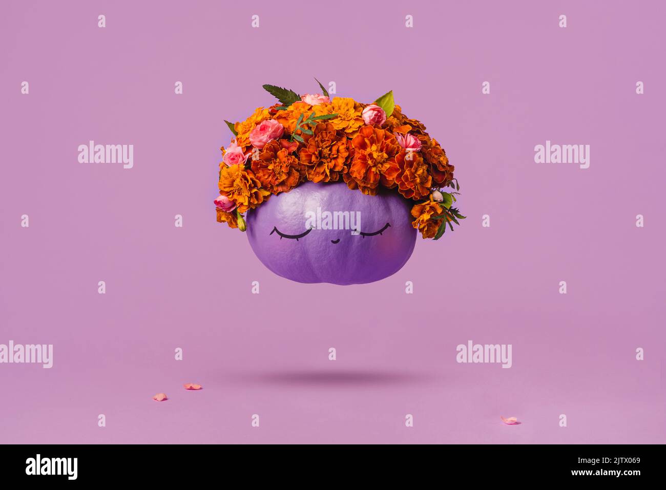 Happy Halloween A purple pumpkin with a funny, kind face and flowers on its head levitates on a pink background. The concept of a positive festive bac Stock Photo