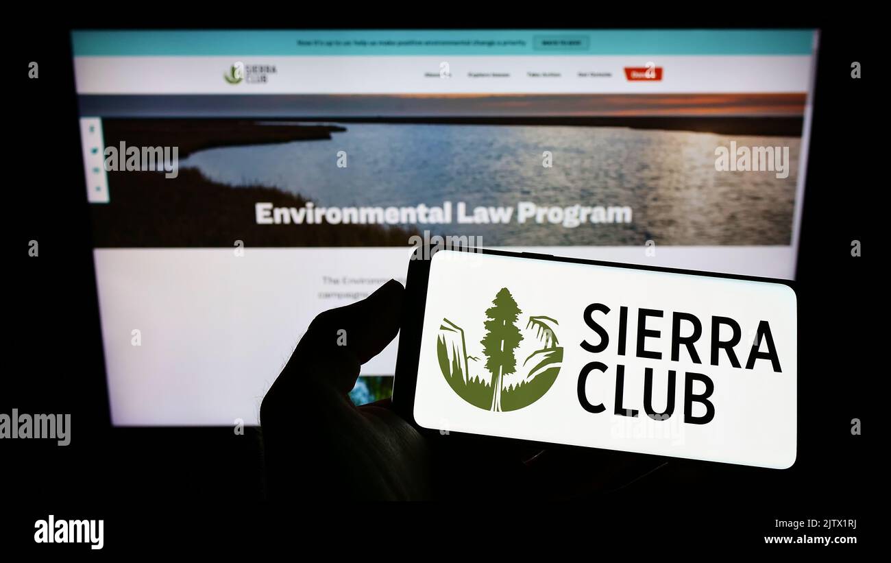 Person holding cellphone with logo of US environmental organization Sierra Club on screen in front of webpage. Focus on phone display. Stock Photo