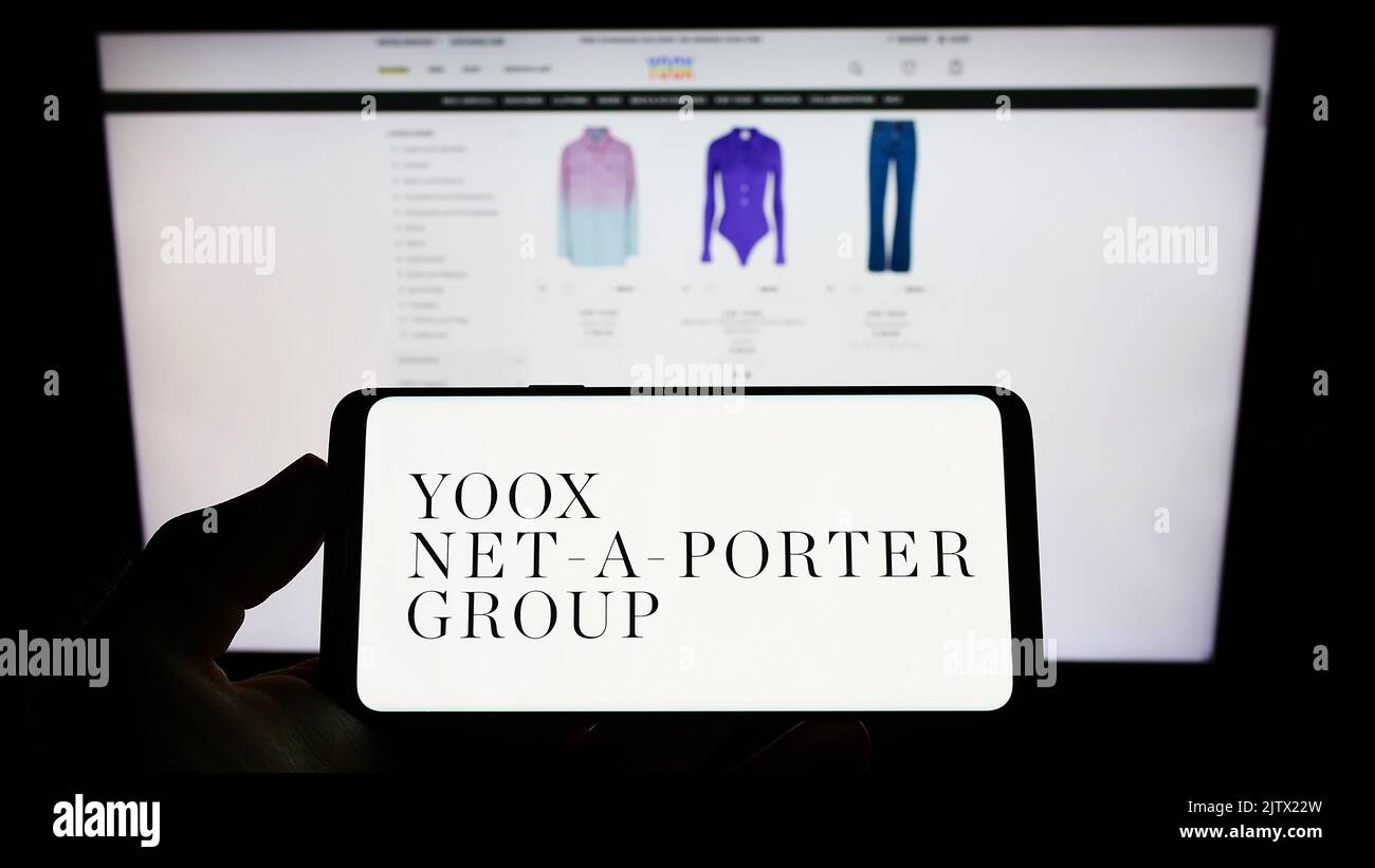 Person holding smartphone with logo of company YOOX Net-a-Porter Group S.p.A. (YNAP) on screen in front of website. Focus on phone display. Stock Photo