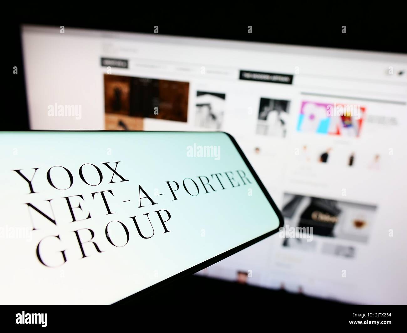 Mobile phone with logo of company YOOX Net-a-Porter Group S.p.A. (YNAP) on screen in front of business website. Focus on center of phone display. Stock Photo