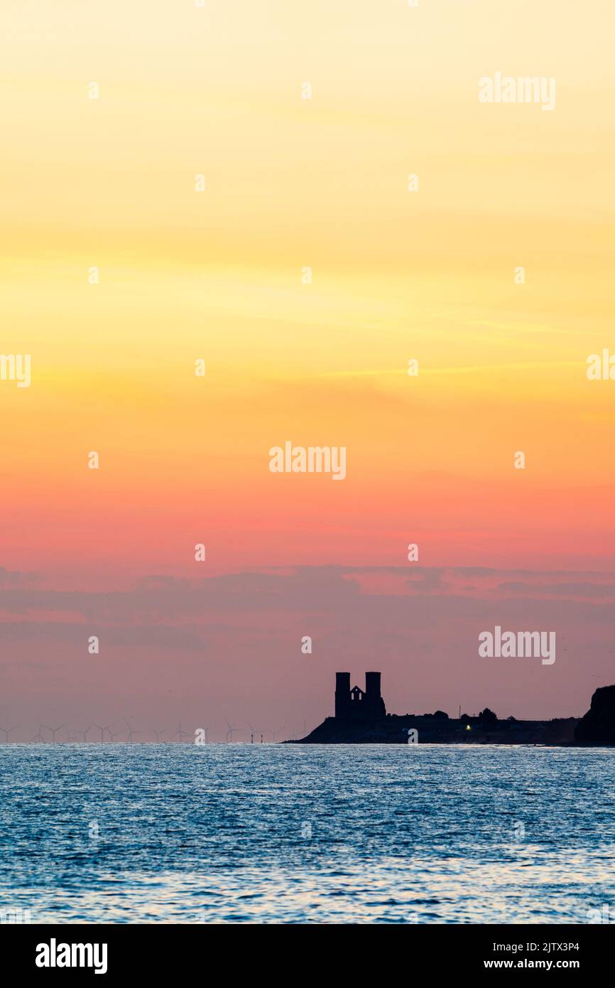 The dawn sky over the sea on the Kent coast at Reculver with the twin towers of the 12th century church silhouetted against the sky. The ruined church is a well-known landmark. Stock Photo