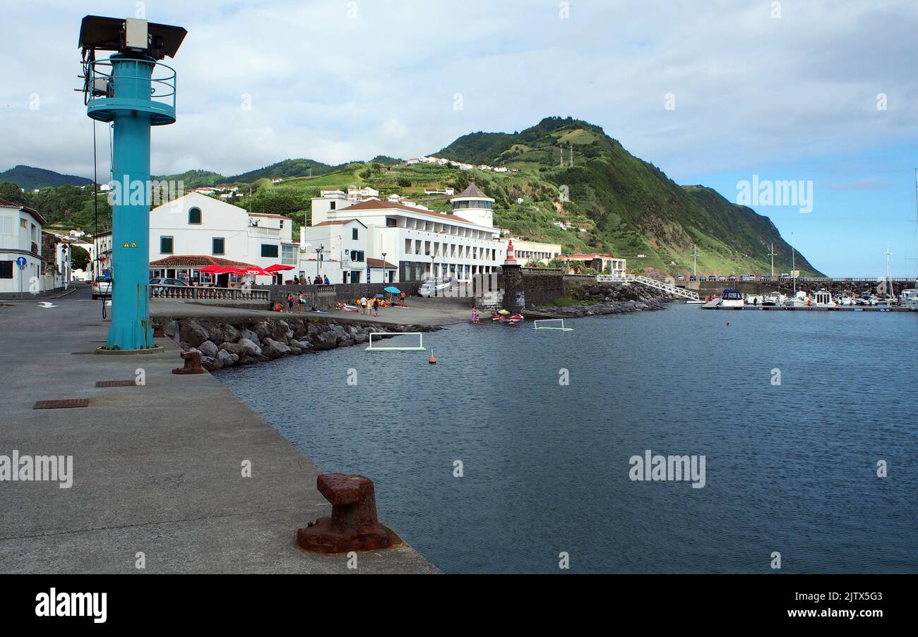 The town's waterfront and marina, rusty mooring cleats on the concrete berth in the forefront, Povoacao, Sao Miguel Island, Azores, Portugal Stock Photo