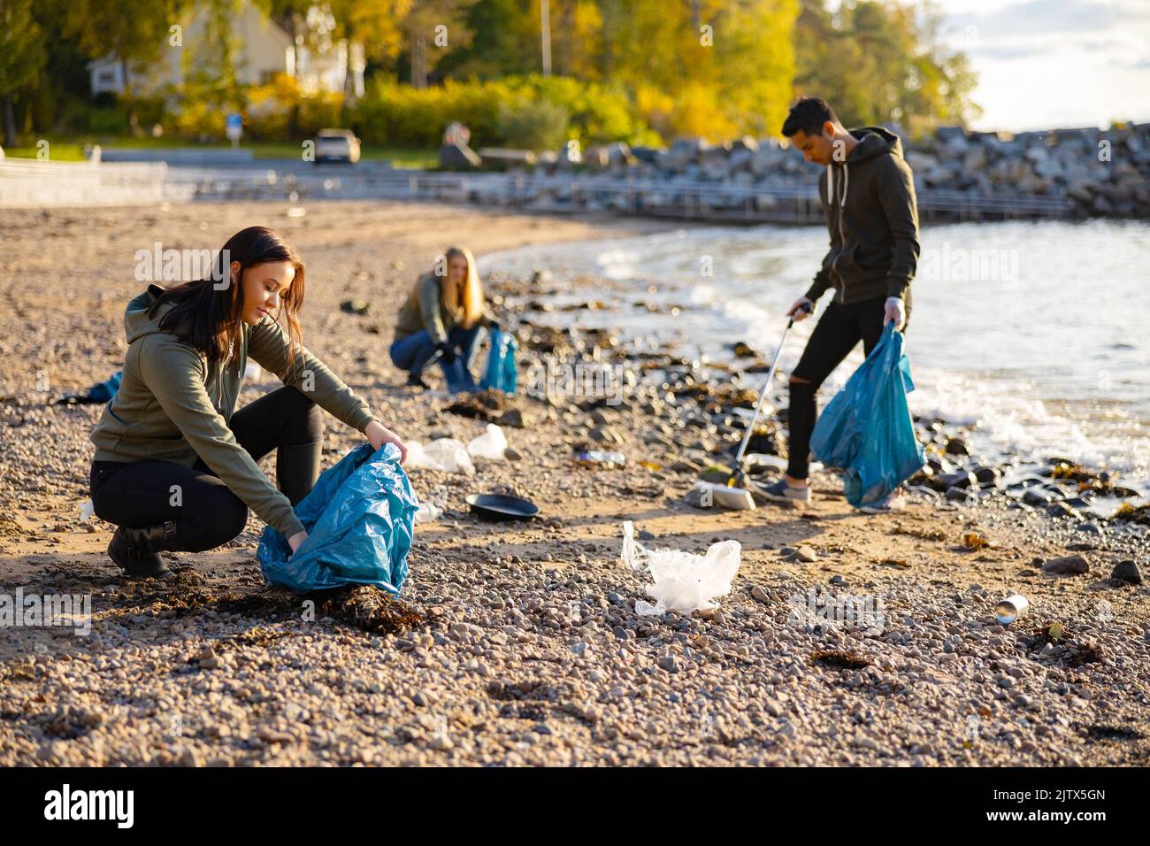Woman in team picking up garbage in bag at beach Stock Photo
