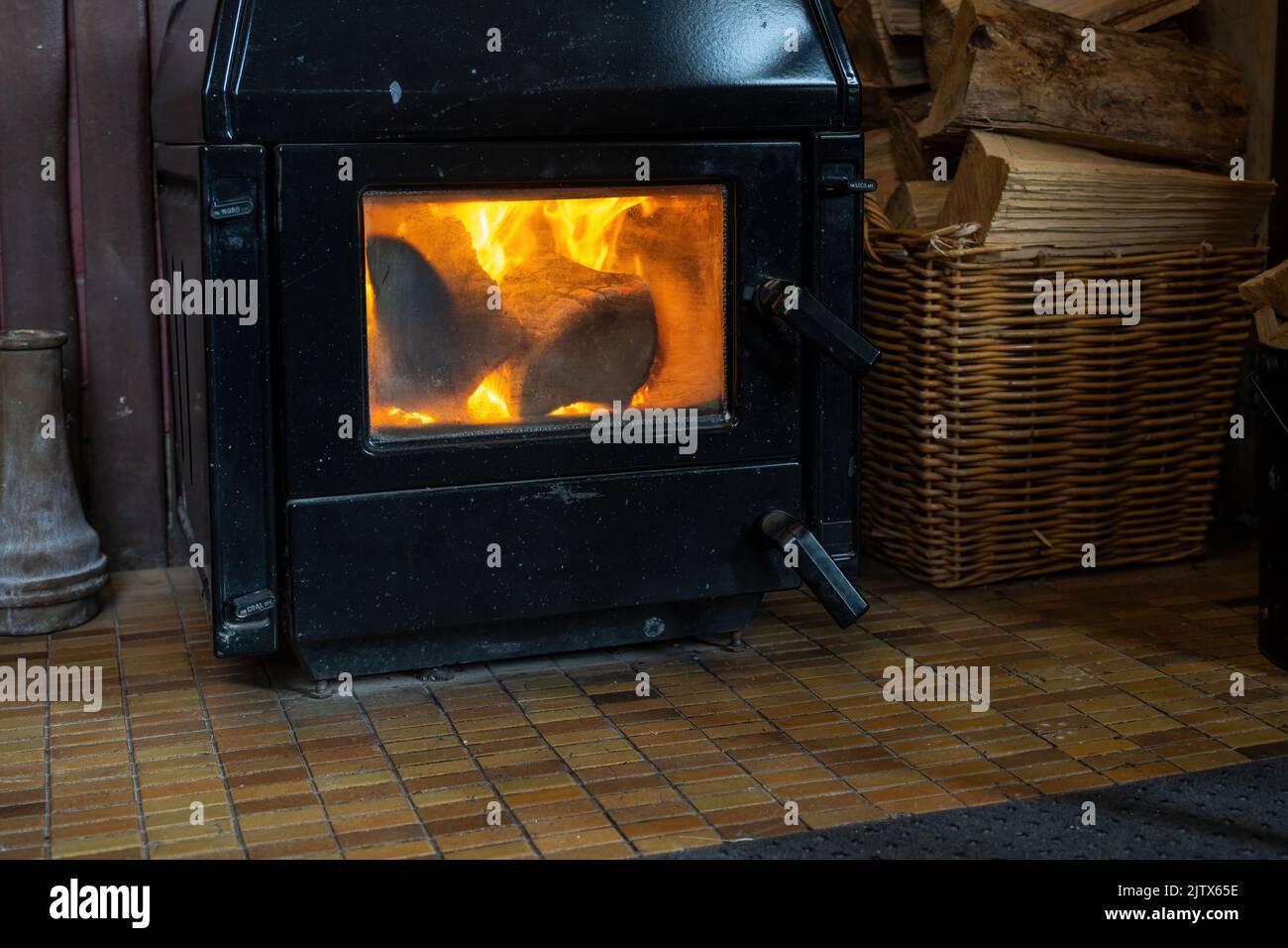 Log burning inside a wood fireplace, firewood in basket. Concept of