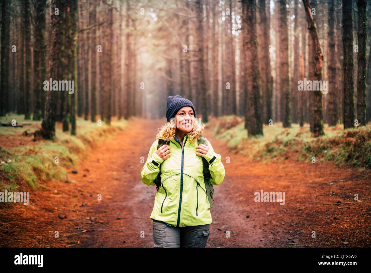 One young woman with a backpack in outdoor excursion leisure activity at the park. Female enjoying nature around smiling and doing trekking path. Stock Photo